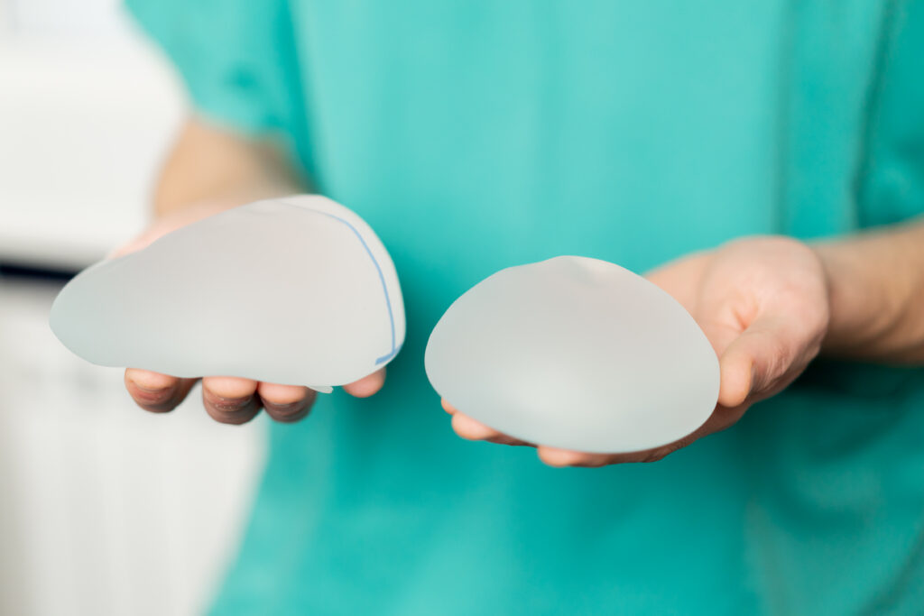 A surgeon holding two breast implants of different volumes.
